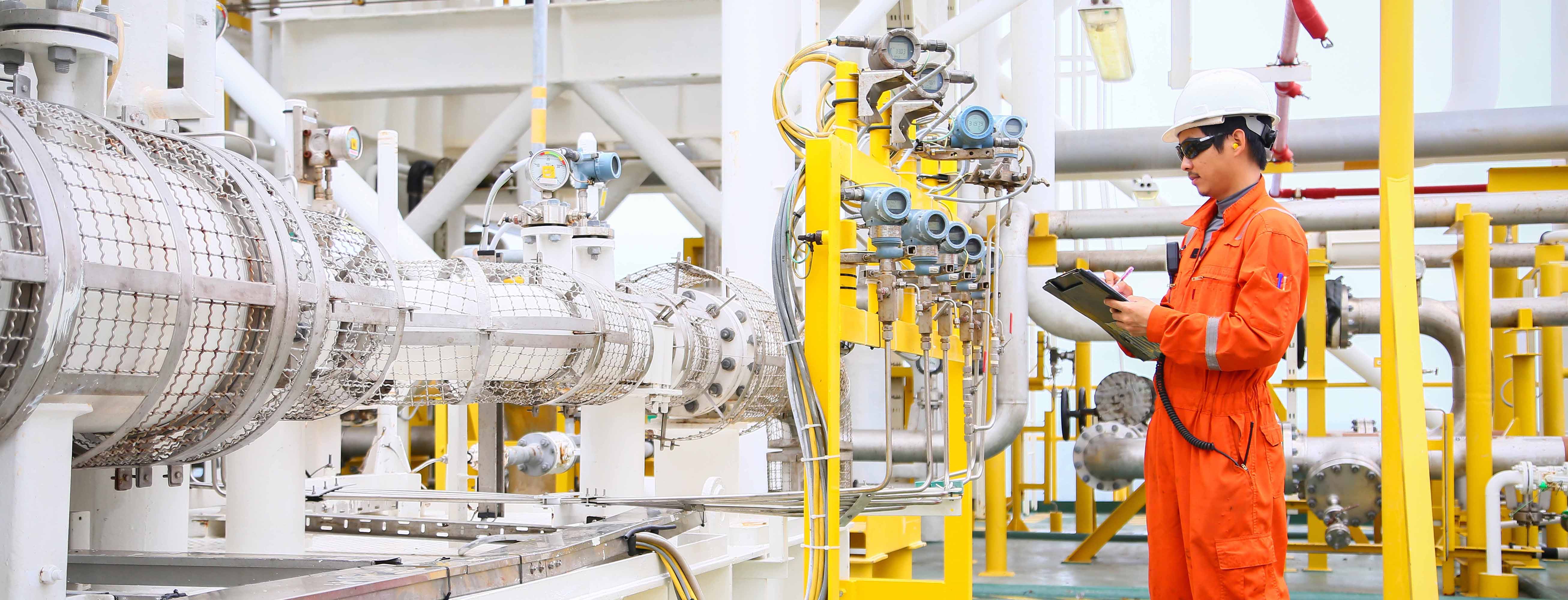 Offshore worker writing on a checklist during inspection of flow control valve gauges